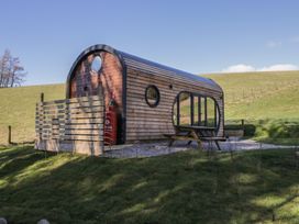 A wooden pod structure with circular windows and a picnic table outside on a grassy hill at Binsey Lodge in Longlands near Caldbeck