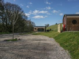 A gravel driveway with small wooden cabins and a tree on a grassy hill at Binsey Lodge Longlands near Caldbeck