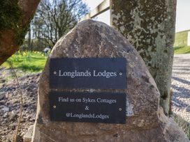 A stone sign with plaques reading Longlands Lodges and Find us on Sykes Cottages and Longlands Lodges outdoors near trees and flowers at Binsey Lodge in Longlands near Caldbeck