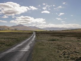 A country road through open fields with hills and clouds in the sky at Binsey Lodge in Longlands near Caldbeck
