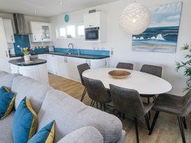A kitchen and dining area with white cabinets a white oval table six gray chairs and a gray sofa with blue and yellow pillows at Bay View in Portreath