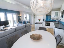 An open plan kitchen and living area with white dining table and chairs a grey sofa kitchen appliances and a television at Bay View in Portreath