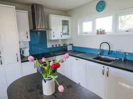 A kitchen with white cabinets black countertops a stainless steel sink a blue backsplash and a vase of flowers on a table at Bay View in Portreath