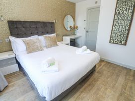 A bedroom with a bed with white linens and pillows a bedside table a dressing table with a round mirror and flowers and a wall art at Bay View Portreath