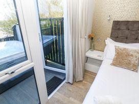 A bedroom with a bed a bedside table with a glass vase and a flower and a door leading to a balcony with a hot tub at Bay View in Portreath