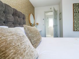 A bedroom with a bed having brown pillows and a gray padded headboard a round mirror on the wall and an open door leading to a bathroom at Bay View in Portreath