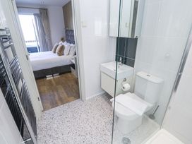 A bathroom with a toilet sink and glass shower door leading to a bedroom with a bed and pillows at Bay View in Portreath
