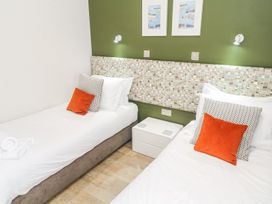 A bedroom with two single beds orange and patterned pillows and a white nightstand between the beds at Bay View in Portreath