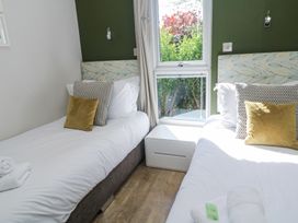 A bedroom with two single beds with patterned headboards and cushions separated by a window and a white bedside table at Bay View in Portreath