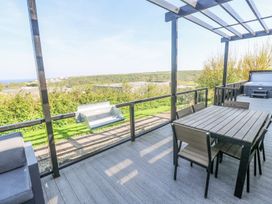 A patio with a dining table and chairs a barbecue grill and a hot tub overlooking greenery and hills at Bay View in Portreath