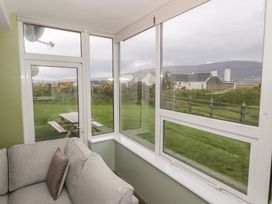 A sunroom with a couch and windows overlooking grass and a picnic table at No.3 Beach Cottages Keel, County Mayo
