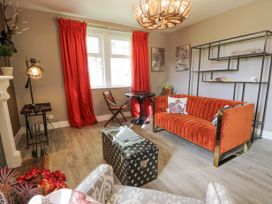 A living room with an orange sofa red curtains a black shelving unit and a patterned armchair at Waterside Lodge near Annan