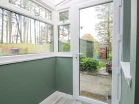 A small enclosed porch with green walls glass door and windows looking out to a garden with green sheds and a wood stack at Waterside Lodge near Annan