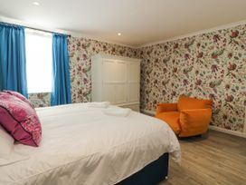 A bedroom with a bed white wardrobe orange chair and blue curtains near Annan