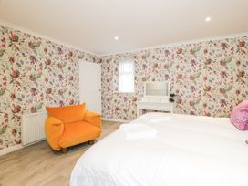 A bedroom with floral wallpaper an orange armchair a white dressing table and a bed with white bedding at Waterside Lodge near Annan