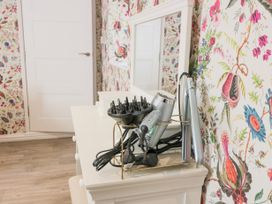 A white dresser with a mirror and hair styling tools including a hair dryer and flat iron on top in a room with floral wallpaper at Waterside Lodge near Annan