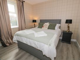 A bedroom with a grey bed, bedside tables with lamps, and a window with curtains at Waterside Lodge near Annan