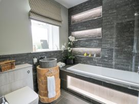 A bathroom with a toilet a wooden vanity with stone sink and a bathtub with built-in shelves and lighting at Waterside Lodge near Annan