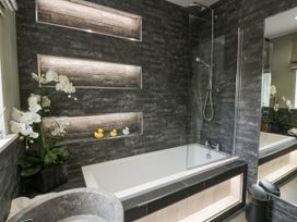 A bathroom with a bathtub shower and white orchids near a window at Waterside Lodge near Annan