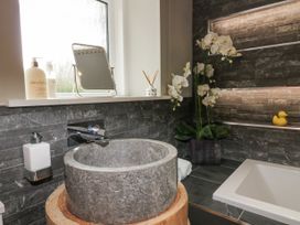 A bathroom with a stone sink on a wooden stand a mirror on the window ledge and a bathtub near orchid flowers at Waterside Lodge near Annan
