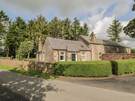 A stone house with a wooden picket fence and tall trees in the background at Waterside Lodge near Annan