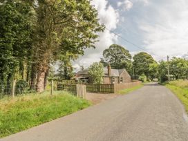 A country road with a stone house and trees along the side at Waterside Lodge near Annan