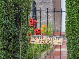 A metal garden gate with a wooden sign reading Waterside Lodge surrounded by greenery and flowers near Annan
