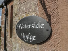A stone wall with a black oval sign reading Waterside Lodge near Annan