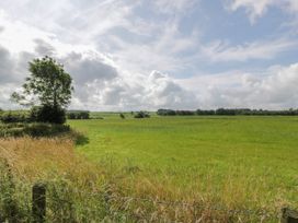 A green field with trees and a wire fence under a cloudy sky at Waterside Lodge near Annan