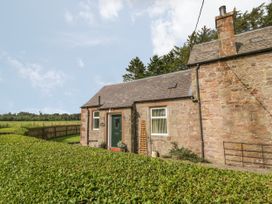 A stone cottage with a green door and garden hedges at Waterside Lodge near Annan