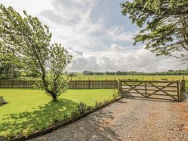 A garden with a tree a gravel driveway and a wooden gate overlooking fields at Waterside Lodge near Annan