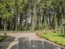 A garden area with a glass table and chair in the foreground a gravel path flower beds a lawn a wooden fence and tall trees in the background at Waterside Lodge near Annan