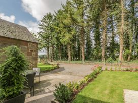A garden with grass and flowers next to a stone building and a gravel path with trees and a wooden gate at Waterside Lodge near Annan