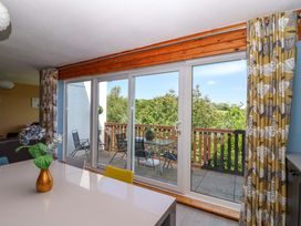 A dining area with a white table and colorful chairs next to sliding glass doors leading to a balcony with outdoor chairs and a table at 37 Tamar St Ann's Chapel near Callington