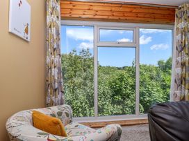 A room with a large window overlooking green trees with a floral armchair and brown cushion next to a black leather chair at 37 Tamar in St Ann's Chapel near Callington