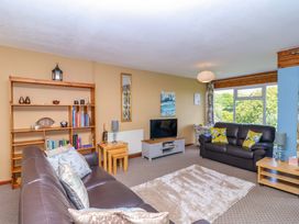 A living room with two brown sofas a wooden bookshelf a flat screen TV and a large window at 37 Tamar in St Ann's Chapel near Callington
