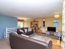 A living room with brown leather sofas a wooden bookshelf a television on a stand and decorative cushions at 37 Tamar in St Ann's Chapel near Callington