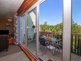 A balcony with a table, chairs, and a view of trees seen through sliding glass doors at 37 Tamar in St Ann's Chapel near Callington