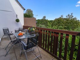 An outdoor balcony with a glass table surrounded by four chairs overlooking trees and greenery at 37 Tamar St Ann's Chapel near Callington