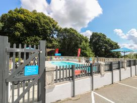 An outdoor swimming pool area with fenced gate umbrellas and chairs surrounded by trees at 37 Tamar in St Ann's Chapel near Callington