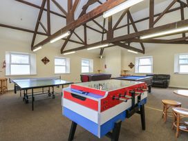 A game room with a foosball table, ping pong table, pool tables, stools, and a leather sofa at 37 Tamar St Ann's Chapel near Callington