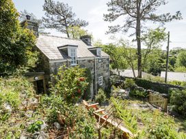A stone cottage with dormer windows surrounded by garden plants trees and outdoor furniture at Pen Y Bryn Bach in Harlech