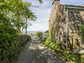 A narrow paved road between stone walls and old stone buildings with greenery and trees near the coast at Pen Y Bryn Bach in Harlech