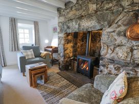 A living room with a stone fireplace wood stove armchairs nesting tables and a rug at Pen Y Bryn Bach in Harlech