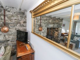 A corner of a living room with a stone wall a television on a wooden cabinet and a large gold-framed mirror reflecting a gray armchair and a stone fireplace at Pen Y Bryn Bach in Harlech