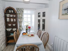 A dining room with a table set for a meal wooden chairs a corner cabinet and a shelf unit at Pen Y Bryn Bach in Harlech