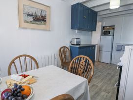 A kitchen dining area with wooden chairs blue cabinets a toaster a fruit bowl and a refrigerator at Pen Y Bryn Bach in Harlech
