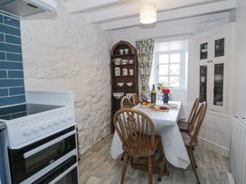 A kitchen with a white stove wooden dining table with chairs and shelves with dishes at Pen Y Bryn Bach in Harlech