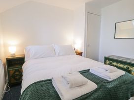 A bedroom with a double bed white bedding green bedspread bedside tables with lamps and a dresser with a mirror at Pen Y Bryn Bach in Harlech