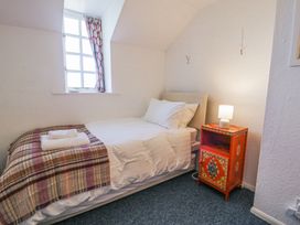 A bedroom with a single bed a patterned throw two towels a window with curtains and a red nightstand with a lamp at Pen Y Bryn Bach in Harlech